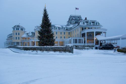 A snowy scene featuring a large yellow hotel with a Christmas tree in front and an American flag flying above.