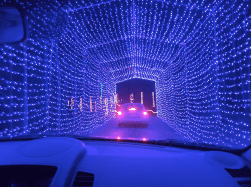 A car drives through a tunnel illuminated with vibrant blue lights, creating a festive atmosphere.