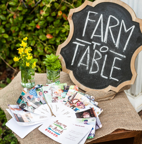 A rustic display featuring a "Farm to Table" sign, flowers, succulents, and a collection of colorful event cards.