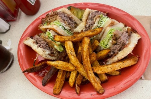 A red plate with a sandwich filled with meat and lettuce, accompanied by golden-brown fries.