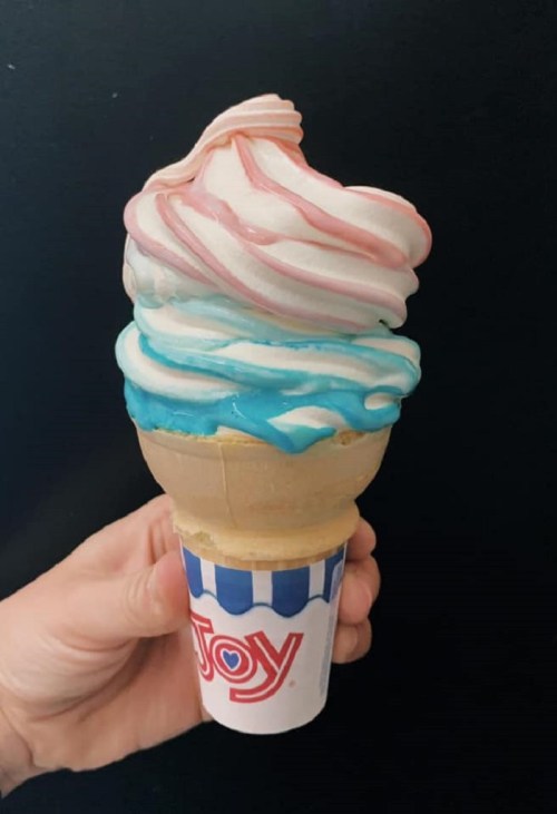 A hand holding a colorful ice cream cone with swirls of pink, white, and blue on top.