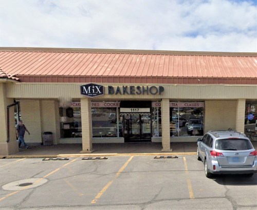 Exterior of MiX Bakeshop with a sign, parking spaces, and a gray car parked in front. Cloudy sky in the background.