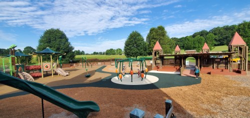 A vibrant playground with slides, swings, and climbing structures, surrounded by green trees and a clear blue sky.