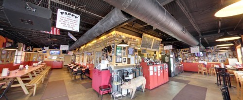 Interior of a casual restaurant with wooden tables, a bar area, and various decorations on the walls.