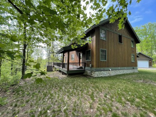 A wooden house surrounded by trees, featuring a porch and grassy area, set in a serene, natural environment.