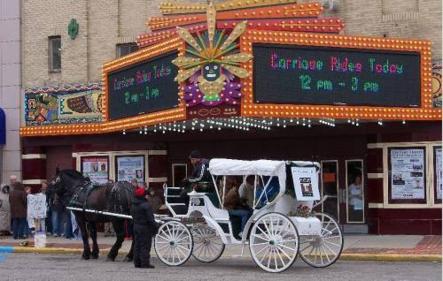 A horse-drawn carriage waits outside a colorful theater with a marquee displaying event times.