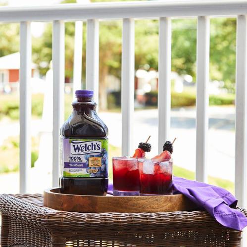 A bottle of Welch's juice on a tray with two glasses of red drinks garnished with fruit, set on a patio.