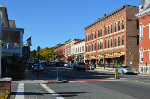 A charming street lined with historic buildings, shops, and trees under a clear blue sky.