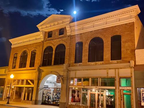 Historic brick building illuminated at night, featuring large windows and a full moon in the sky above.