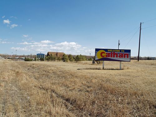 A welcome sign for Callahan, with a grassy area and a few buildings in the background under a partly cloudy sky.