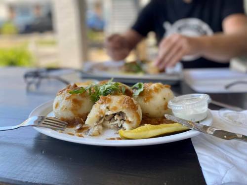 A plate of stuffed dumplings with sauce, garnished with green onions, alongside a pickle and dipping sauce.
