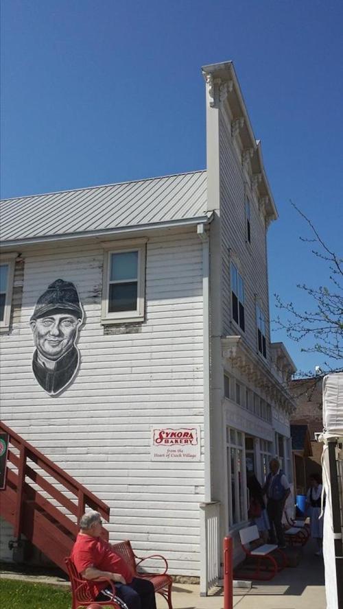 A white building with a mural of a man on the side, featuring a blue sky and people nearby.
