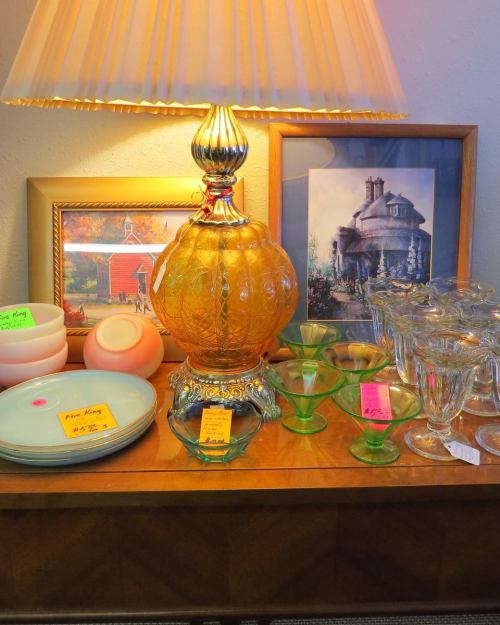 A vintage lamp, colorful glassware, and framed artwork displayed on a wooden table.