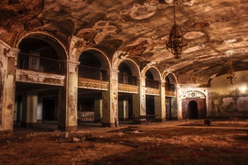 An abandoned, decaying interior with arched columns, peeling paint, and dim lighting, evoking a sense of history.