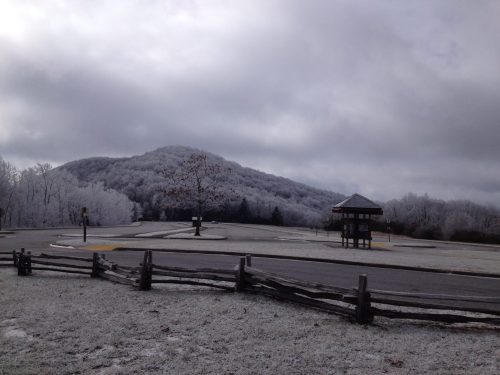 Frost-covered landscape with a mountain in the background, a gazebo, and a wooden fence under a cloudy sky.