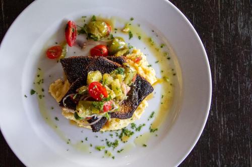 A plate of blackened fish topped with colorful vegetables and cherry tomatoes, served on a bed of creamy mashed potatoes.