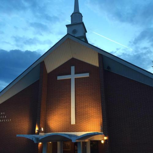A church building with a prominent cross on the facade, illuminated against a twilight sky.