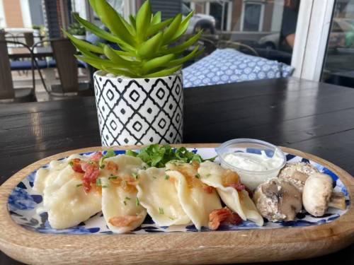 A wooden platter with dumplings, a small bowl of sauce, and mushrooms, alongside a potted succulent plant.