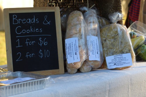 A display of breads and cookies for sale, with a chalkboard sign listing prices: 1 for $6, 2 for $10.