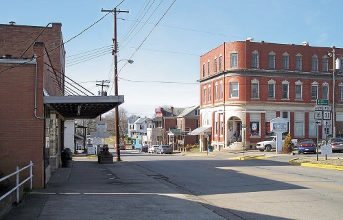 A small town street featuring brick buildings, shops, and power lines under a clear blue sky.