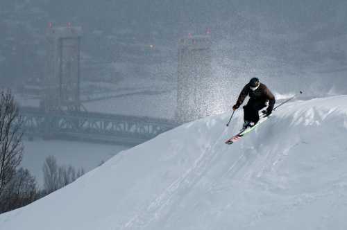 A skier descends a snowy slope with a bridge visible in the background, surrounded by a misty atmosphere.