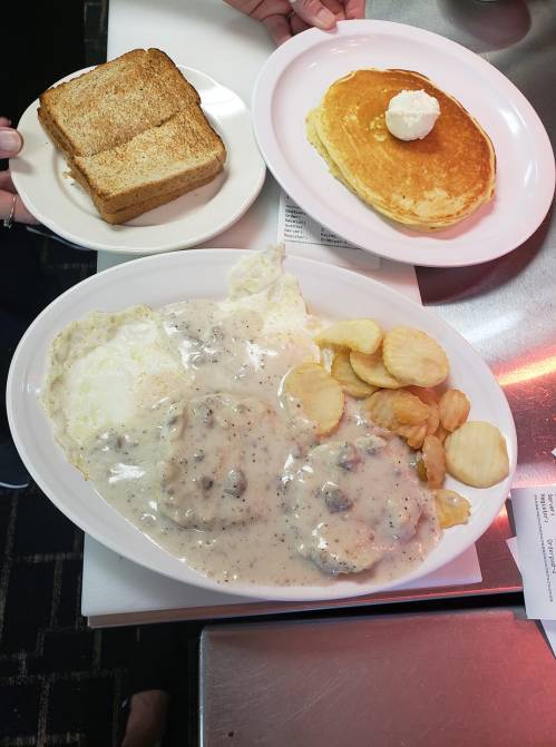A plate with biscuits and gravy, two eggs, and potato chips, alongside a plate of pancakes with butter.