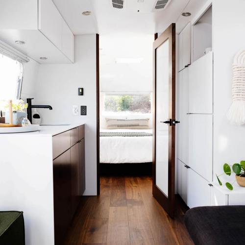 A modern, minimalist interior of a small living space with a kitchen area and a doorway leading to a bedroom.