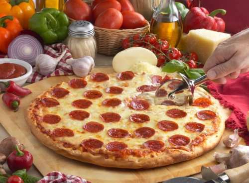 A freshly baked pepperoni pizza on a wooden board, surrounded by fresh vegetables and ingredients.