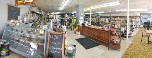 A cozy store interior with shelves of goods, a wooden counter, and a display case filled with treats.