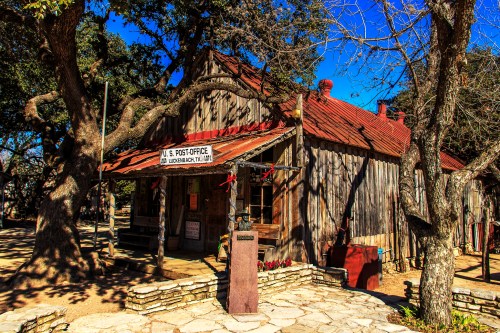 Historic wooden post office building with a red roof, surrounded by trees and a clear blue sky.