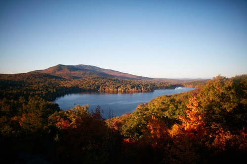 A serene lake surrounded by vibrant autumn foliage and mountains under a clear blue sky.
