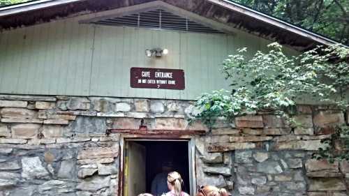 A stone building with a sign reading "Cave Entrance" and people entering the cave. Trees surround the entrance.