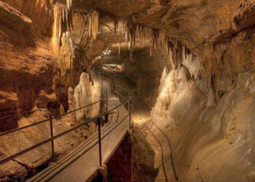 A dimly lit cave with stalactites and stalagmites, featuring a walkway along the rocky terrain.