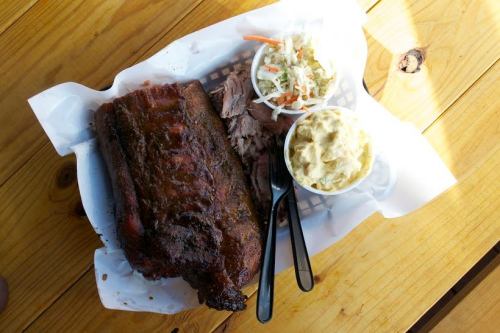 A plate of barbecue ribs with pulled pork, coleslaw, and potato salad on a wooden table.