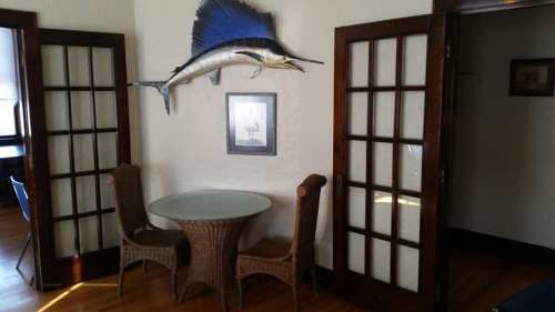 A small dining area with a round glass table and two chairs, featuring a mounted fish on the wall.