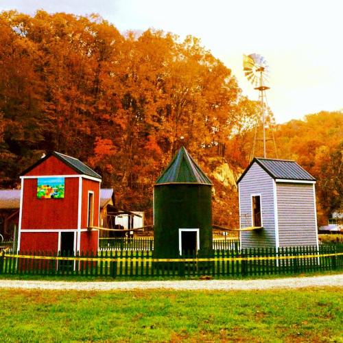 Three colorful barns with a windmill in the background, surrounded by trees in autumn foliage.