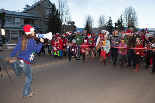 A festive crowd in Santa hats prepares to run, while a person with a megaphone starts the race.