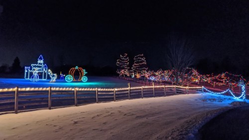 Colorful holiday lights illuminate a snowy landscape, featuring a castle and a pumpkin carriage against a dark night sky.