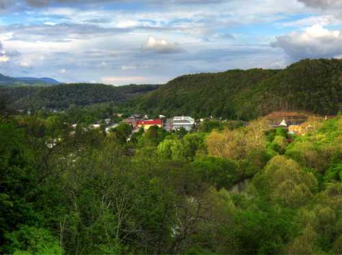 A scenic view of a lush green valley with hills, trees, and a small town nestled among the landscape under a cloudy sky.