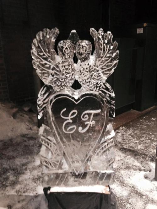 An intricately carved ice sculpture featuring two birds and a heart with the initials "EF" engraved in it.