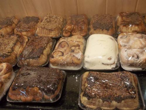 A display of various baked goods, including cinnamon rolls and pastries, all covered in plastic wrap.