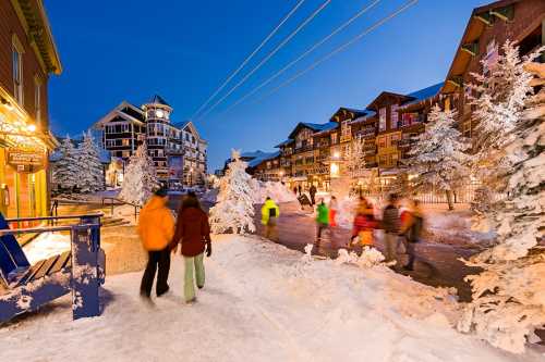 A snowy street scene at dusk, with people walking past charming buildings and frosted trees.