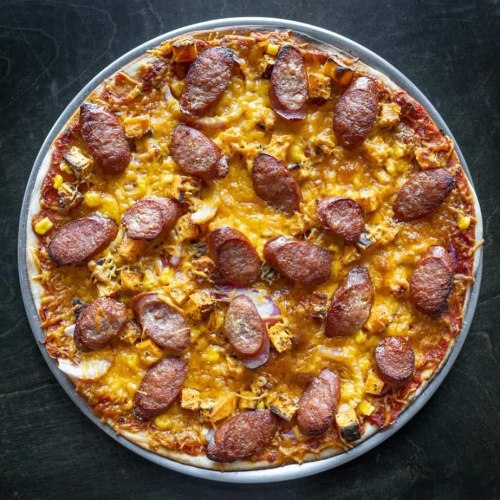 A round pizza topped with slices of sausage, cheese, and various toppings on a dark surface.