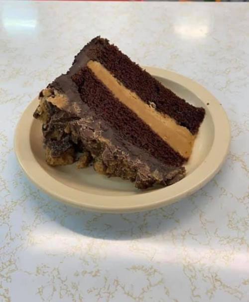 A slice of chocolate cake with layers of chocolate and peanut butter frosting on a beige plate.