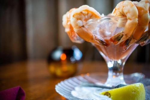 A glass dish filled with shrimp cocktail, garnished with lime, on a wooden table with a blurred background.