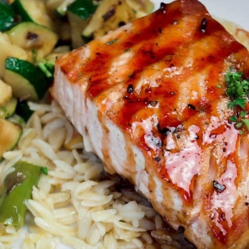 Grilled salmon fillet on a bed of orzo, served with sautéed zucchini and herbs.
