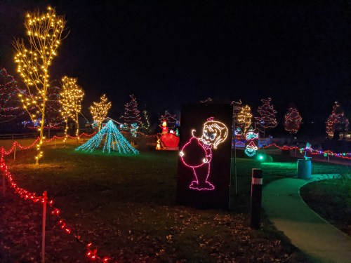 Colorful holiday lights illuminate a park at night, featuring festive decorations and a glowing character display.