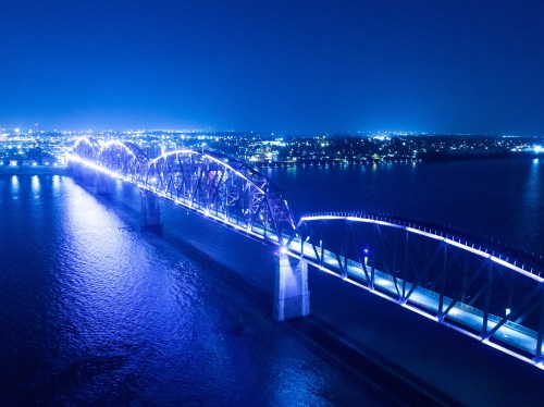 Aerial view of a brightly lit bridge over water at night, with city lights in the background.