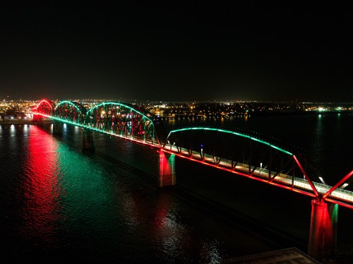 A brightly lit bridge at night, adorned with red and green lights reflecting on the water below.