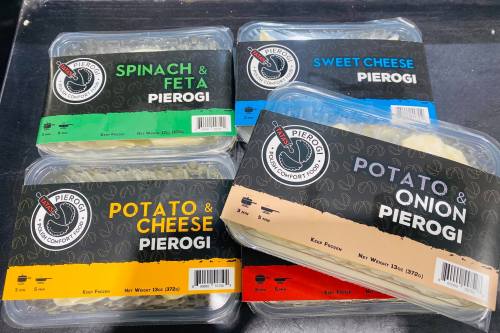 Four packages of pierogi featuring spinach & feta, sweet cheese, and potato & onion flavors, displayed on a black surface.